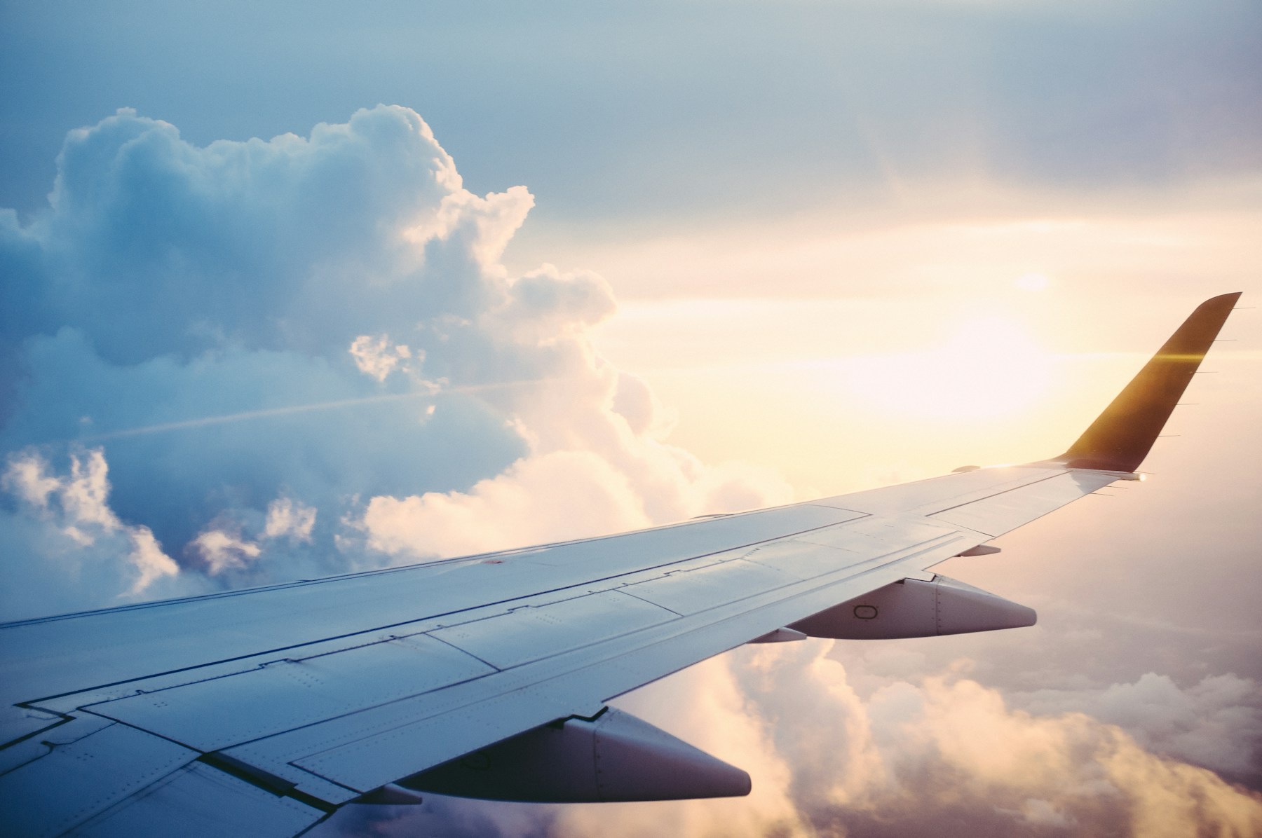 An airplane wing above sunlit clouds